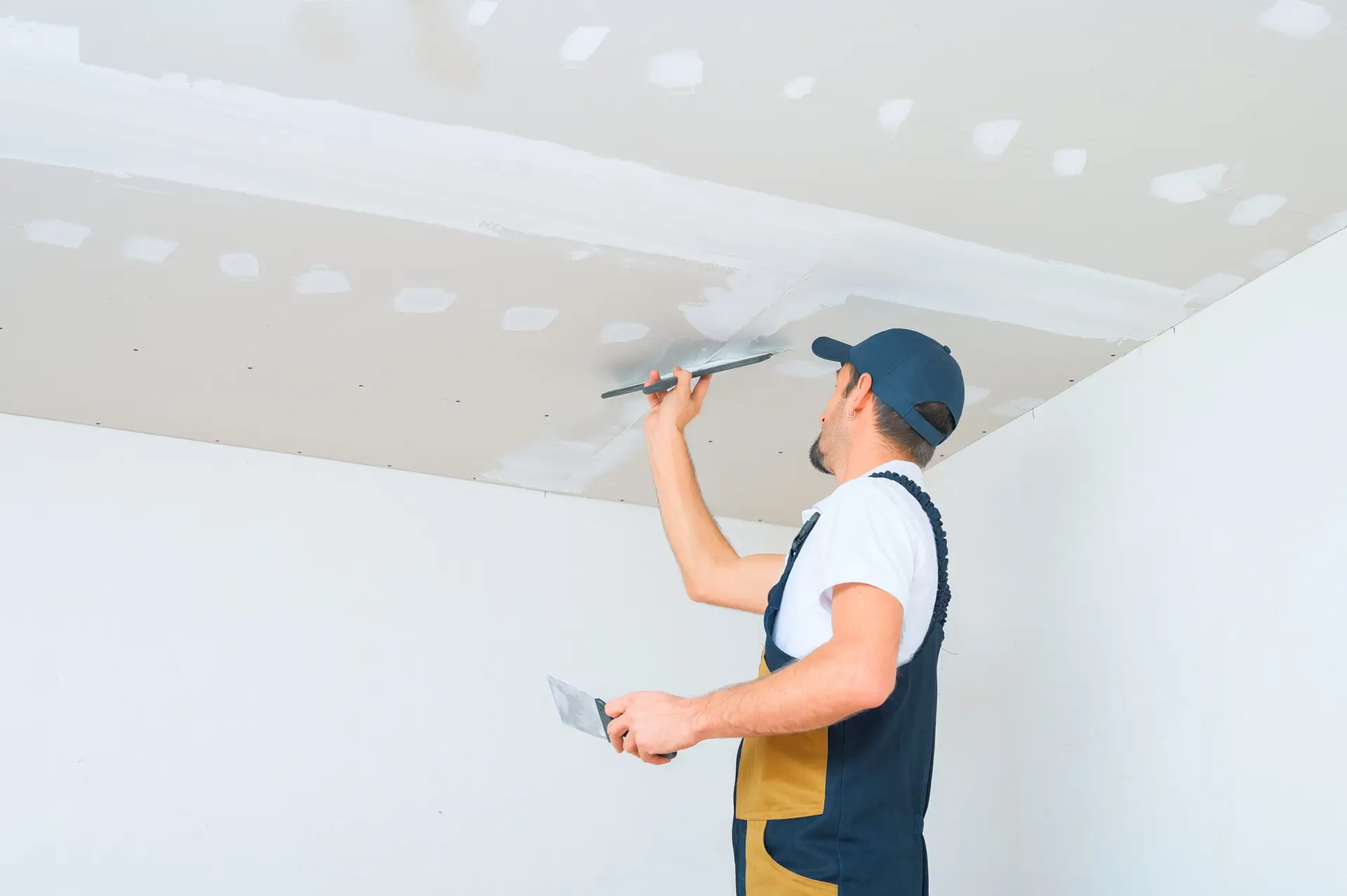 A uniformed worker applies putty to the drywall ceiling in Dallas GA.